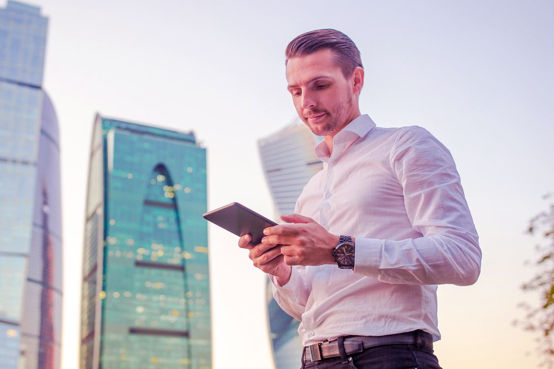 Image of a man looking at his mobile phone, standing outside surrounded by buildings